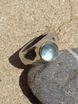 Ein runder, himmelblau strahlender Edeltopascabochon in Gold gefasst auf einem Silberring