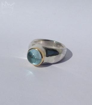 Preview: Ein runder, himmelblau strahlender Edeltopascabochon in Gold gefasst auf einem Silberring