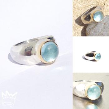 Preview: Ein runder, himmelblau strahlender Edeltopascabochon in Gold gefasst auf einem Silberring