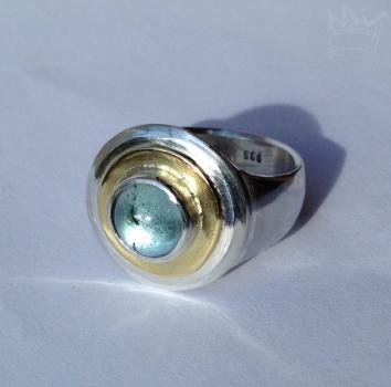 Preview: Ein wundervoller, zart hellblauer Edeltopas, eingebettet in ein goldenes Band, gefasst in Silber auf einer gegossenen Ringschiene ebenfalls aus 935er Silber.
