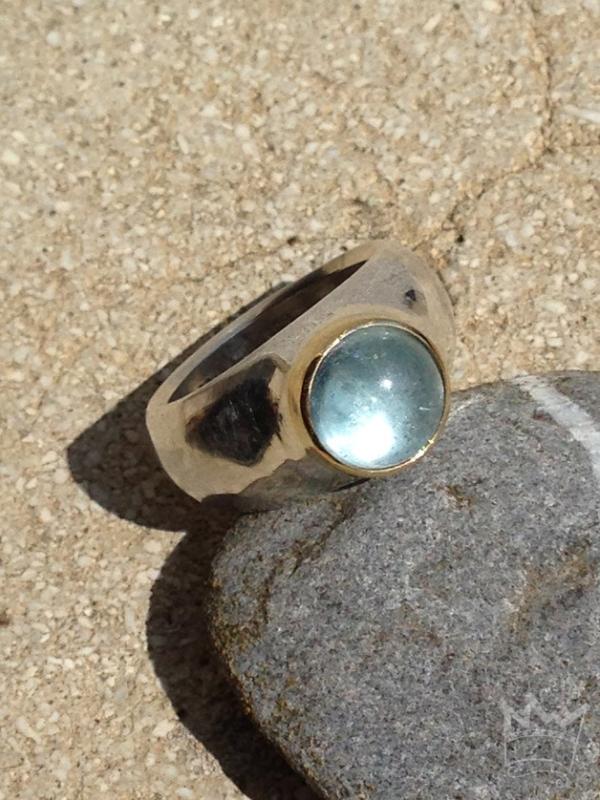 Ein runder, himmelblau strahlender Edeltopascabochon in Gold gefasst auf einem Silberring