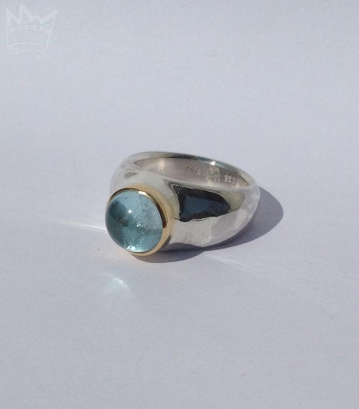 Ein runder, himmelblau strahlender Edeltopascabochon in Gold gefasst auf einem Silberring