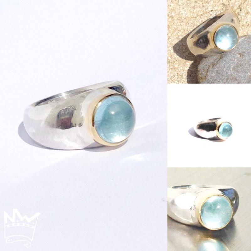 Ein runder, himmelblau strahlender Edeltopascabochon in Gold gefasst auf einem Silberring