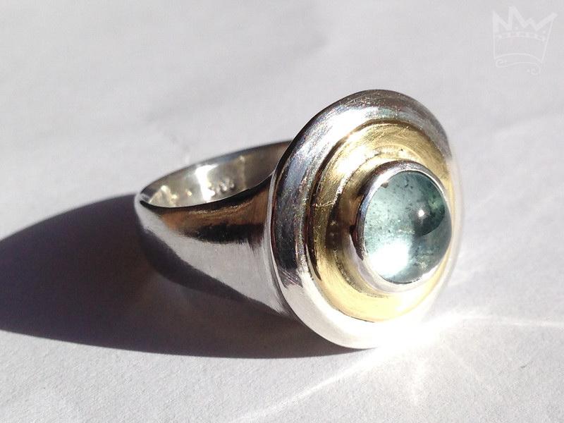 Ein wundervoller, zart hellblauer Edeltopas, eingebettet in ein goldenes Band, gefasst in Silber auf einer gegossenen Ringschiene ebenfalls aus 935er Silber.