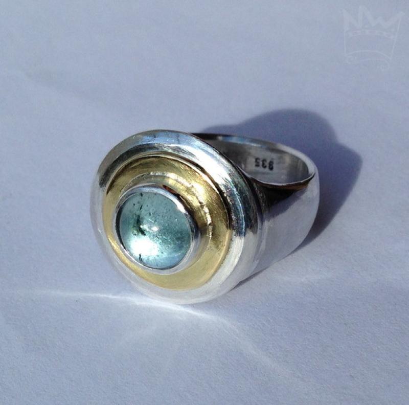 Ein wundervoller, zart hellblauer Edeltopas, eingebettet in ein goldenes Band, gefasst in Silber auf einer gegossenen Ringschiene ebenfalls aus 935er Silber.