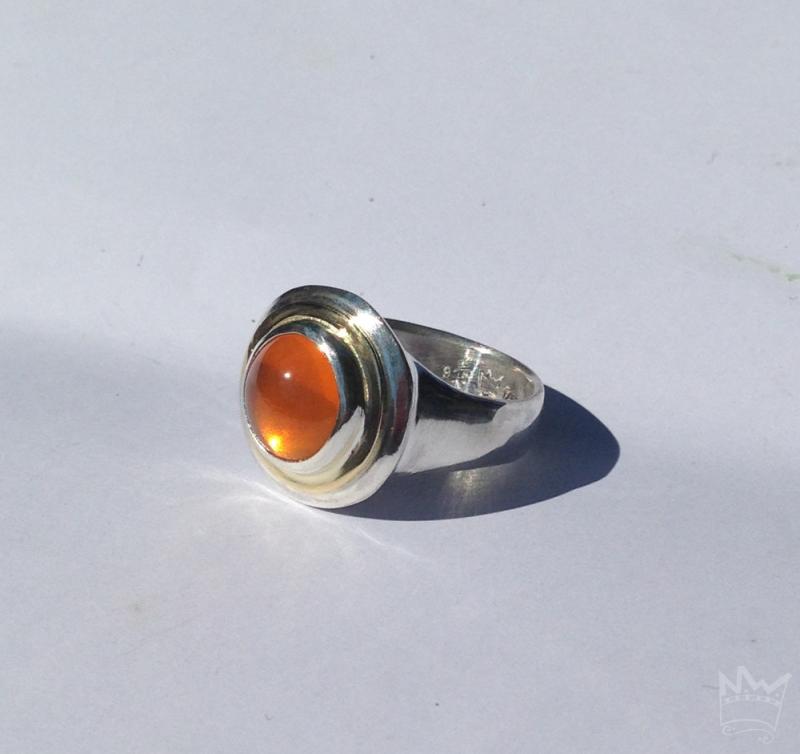 Der Feueropalcabochon ist in Silber gefasst und wird von einem goldenen Band umlaufen.
