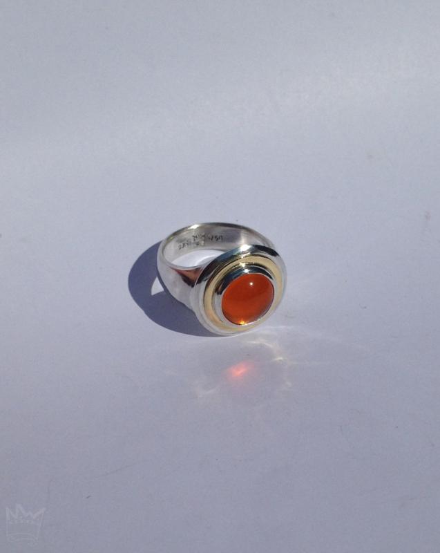 Der Feueropalcabochon ist in Silber gefasst und wird von einem goldenen Band umlaufen.