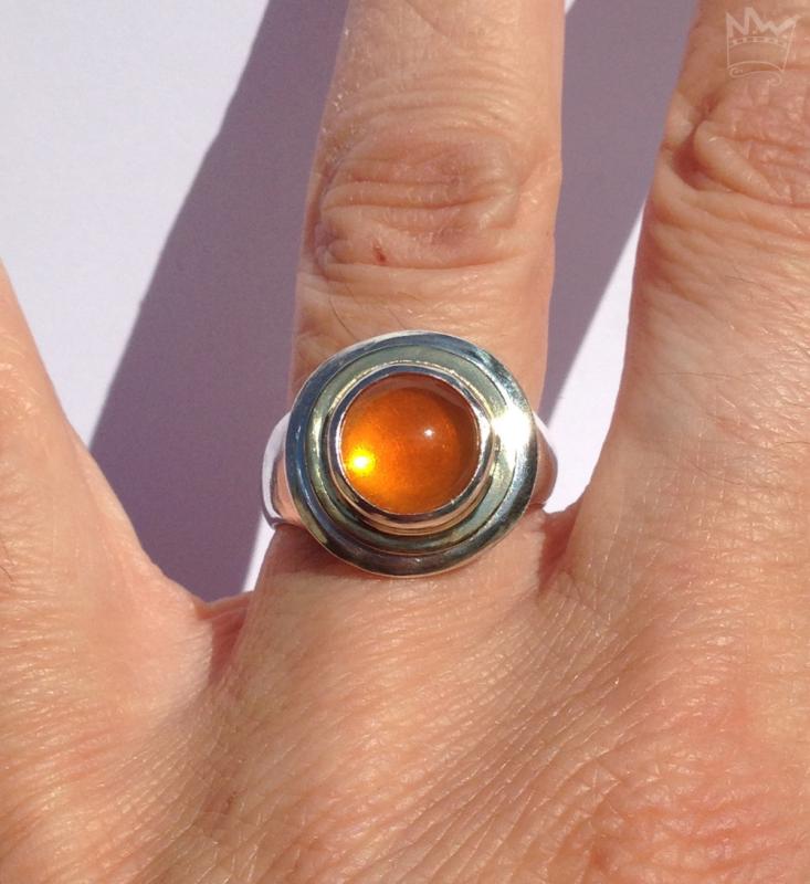 Der Feueropalcabochon ist in Silber gefasst und wird von einem goldenen Band umlaufen.