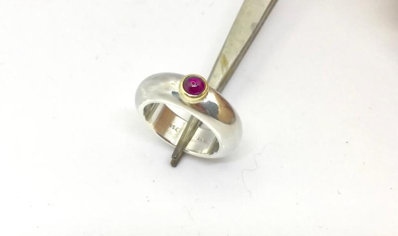 Ein runder rosaner Rhodolithcabochon ist in einer Goldfassung aus 750er Gold gefasst und sitzt auf einer kräftigen und aus einem Stück gegossenen Ringschiene aus 935er Silber.