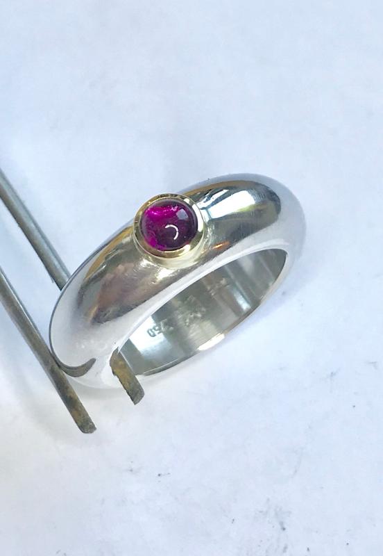 Ein runder rosaner Rhodolithcabochon ist in einer Goldfassung aus 750er Gold gefasst und sitzt auf einer kräftigen und aus einem Stück gegossenen Ringschiene aus 935er Silber.