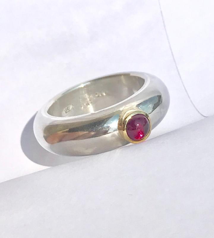 Ein runder rosaner Rhodolithcabochon ist in einer Goldfassung aus 750er Gold gefasst und sitzt auf einer kräftigen und aus einem Stück gegossenen Ringschiene aus 935er Silber.