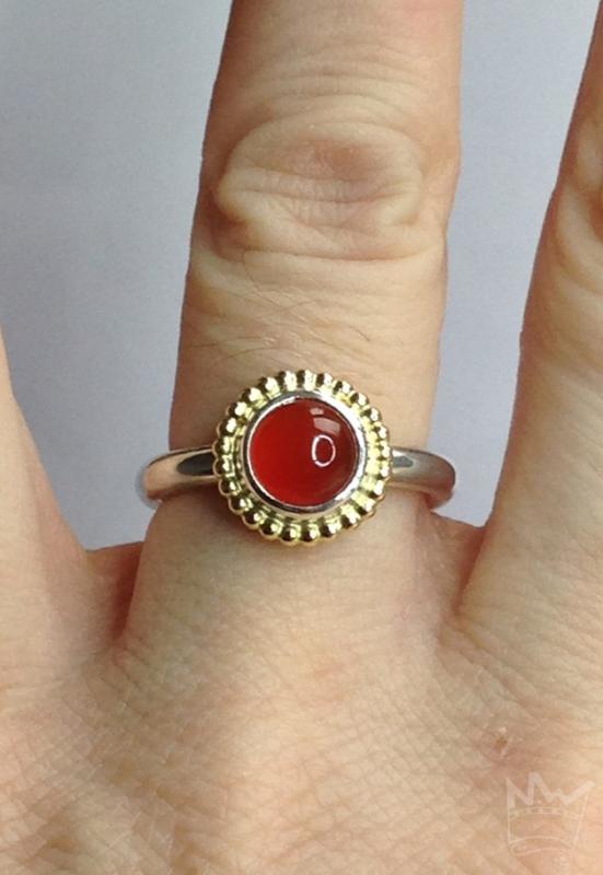 Ein runder, zinnoberroter, wunderschöner Karneol, sitzt auf einem feinen Silbertellerchen und ist ebenfalls in Sterlingsilber gefasst. Um die Fassung läuft ein feiner Kugelkranz aus 18kt Gelbgold.